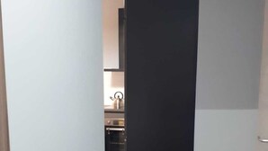 Un pasillo estrecho con una puerta negra al final, que da a una cocina con electrodomésticos modernos.