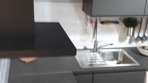 Una cocina moderna con un lavamanos de acero inoxidable, una tetera y una encimera negra.