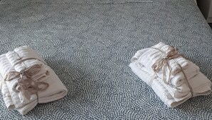 Una cama bien hecha con una colcha estampada, dos almohadas y dos toallas dobladas con cintas.