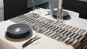 Un comedor moderno con mantel individual a cuadros, velas, copas de vino y una estantería para vinos montada en la pared.