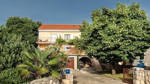 A two-story building with a stone entrance, a staircase, and a large tree in front.