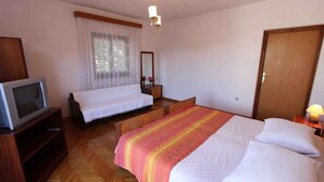 A hotel room with a bed, a TV, a wooden wardrobe, a nightstand, a lamp, and a window with curtains.
