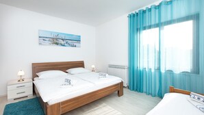 Ein Schlafzimmer mit einem hölzernen Bett, zwei Nachttischen mit Lampen, einer Heizung und einem großen Fenster mit blauen Vorhängen.