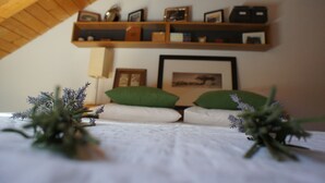 Een gezellige kamer met een schuine kap, een bed met groene en witte kussens, een ingelijst beeld aan de muur en een plank met diverse spullen.
