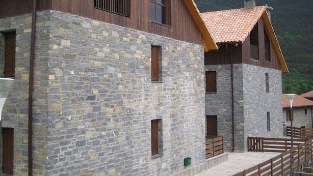 Een gebouw van steen met houten balkons en een pannendak, omgeven door een bergachtig landschap.