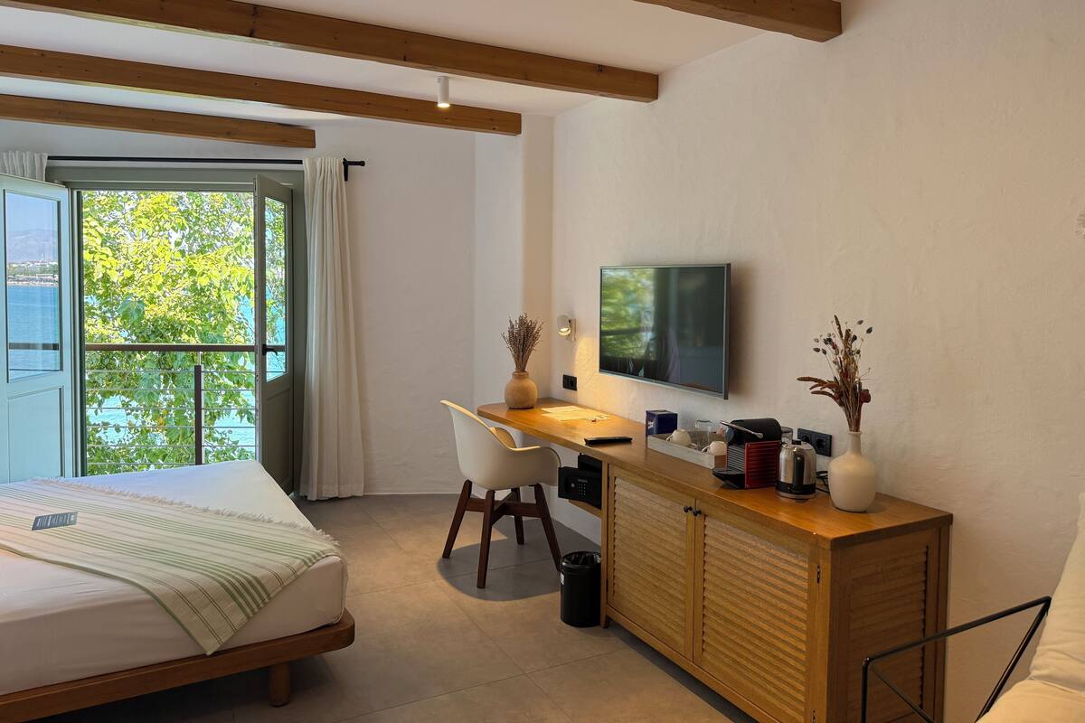A modern bedroom with a bed, a desk, a television, and a view of the outdoors.