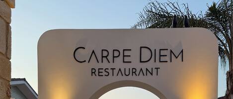 An entrance to Carpe Diem Restaurant with a clear pathway leading to the dining area, surrounded by greenery and a decorative floor pattern.