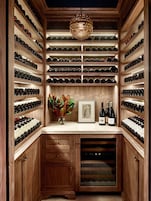 Una bodega con estantes de madera y un botellero, un jarrón con flores y una botella de vino sobre la encimera.