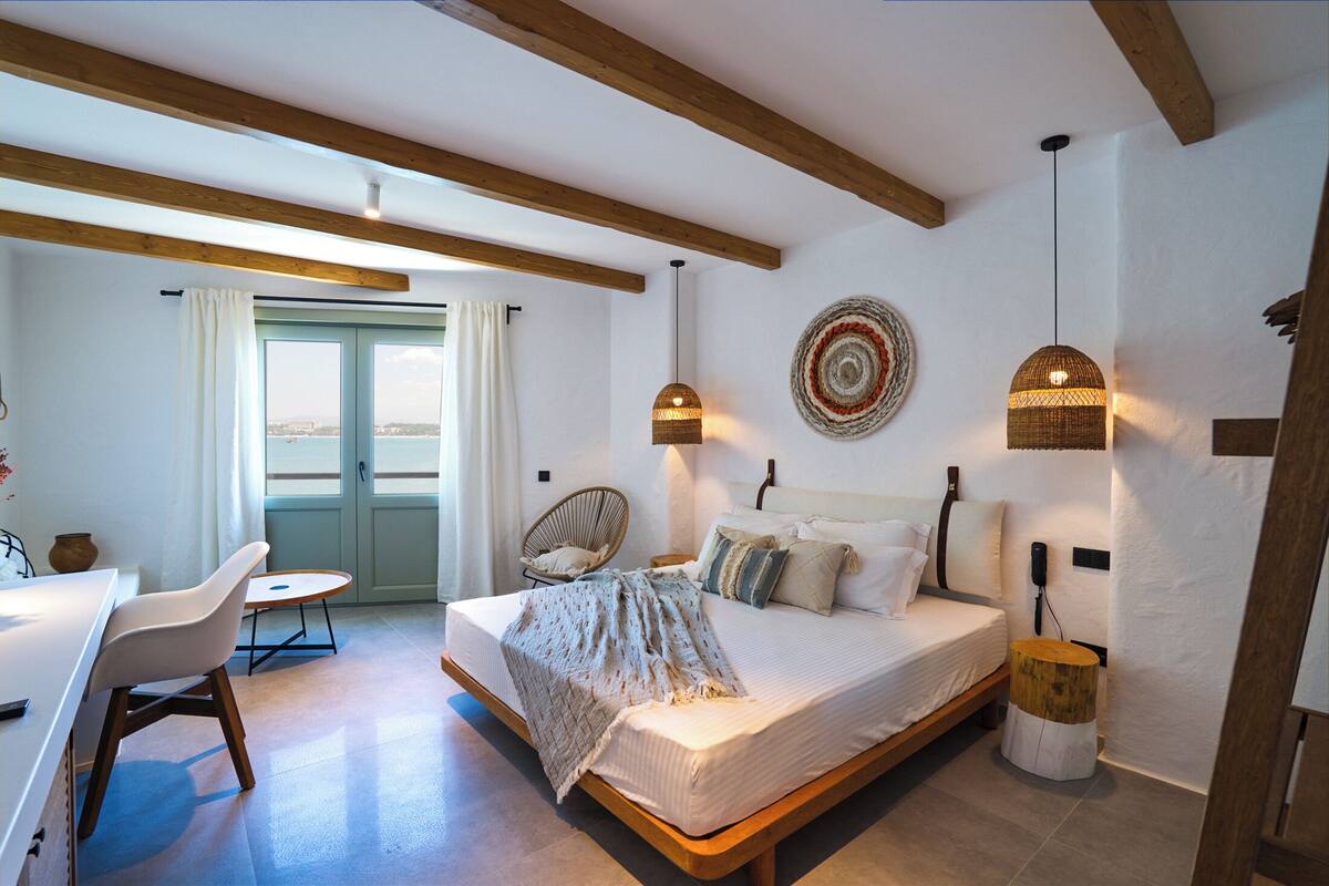 A bedroom with a bed, bedside table, chair, and a view of the outdoors.