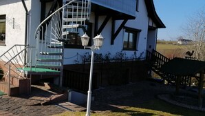Un edificio con una escalera de caracol, una terraza de madera y una estatua de gallo.