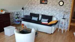 Una sala de estar moderna con un sofá blanco, cojines negros y grises, una mesa de centro de vidrio y una pared con diseño de ladrillo.