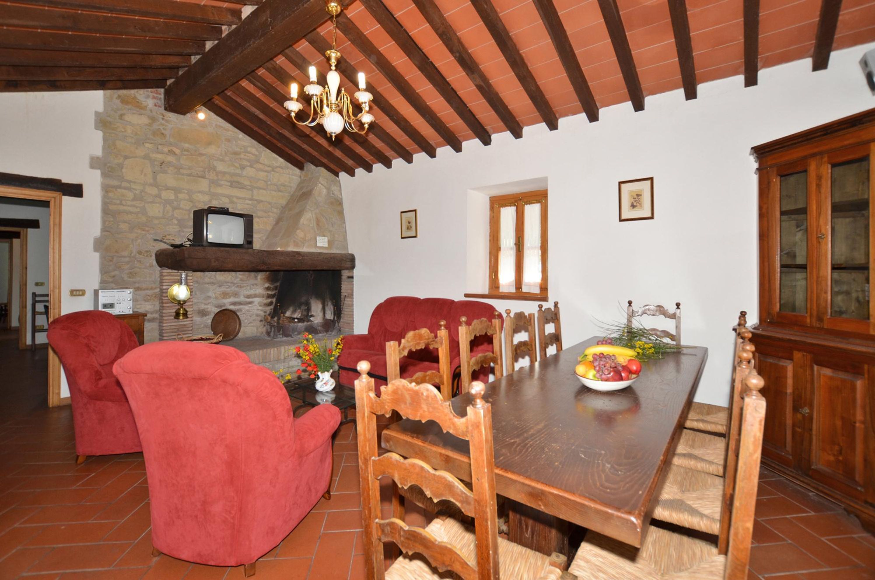A dining area with a wooden table, red upholstered chairs, a chandelier, and a stone fireplace.