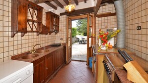 A kitchen with wooden cabinets, a double sink, a stove, and a view to an outdoor patio. - Villa Piombona in Anghiari (Anghiari)