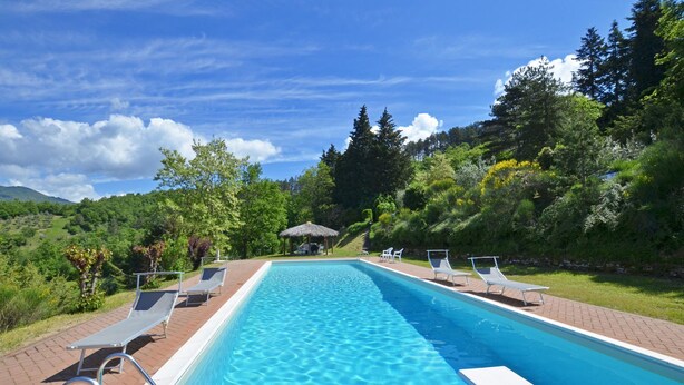 A rectangular swimming pool with clear blue water, surrounded by a brick patio. There are lounge chairs and a small gazebo in the background. - Villa Piombona in Anghiari (Anghiari)