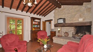 A cozy living room with red armchairs, a fireplace, a bookshelf, and a television. - Villa Piombona in Anghiari (Anghiari)