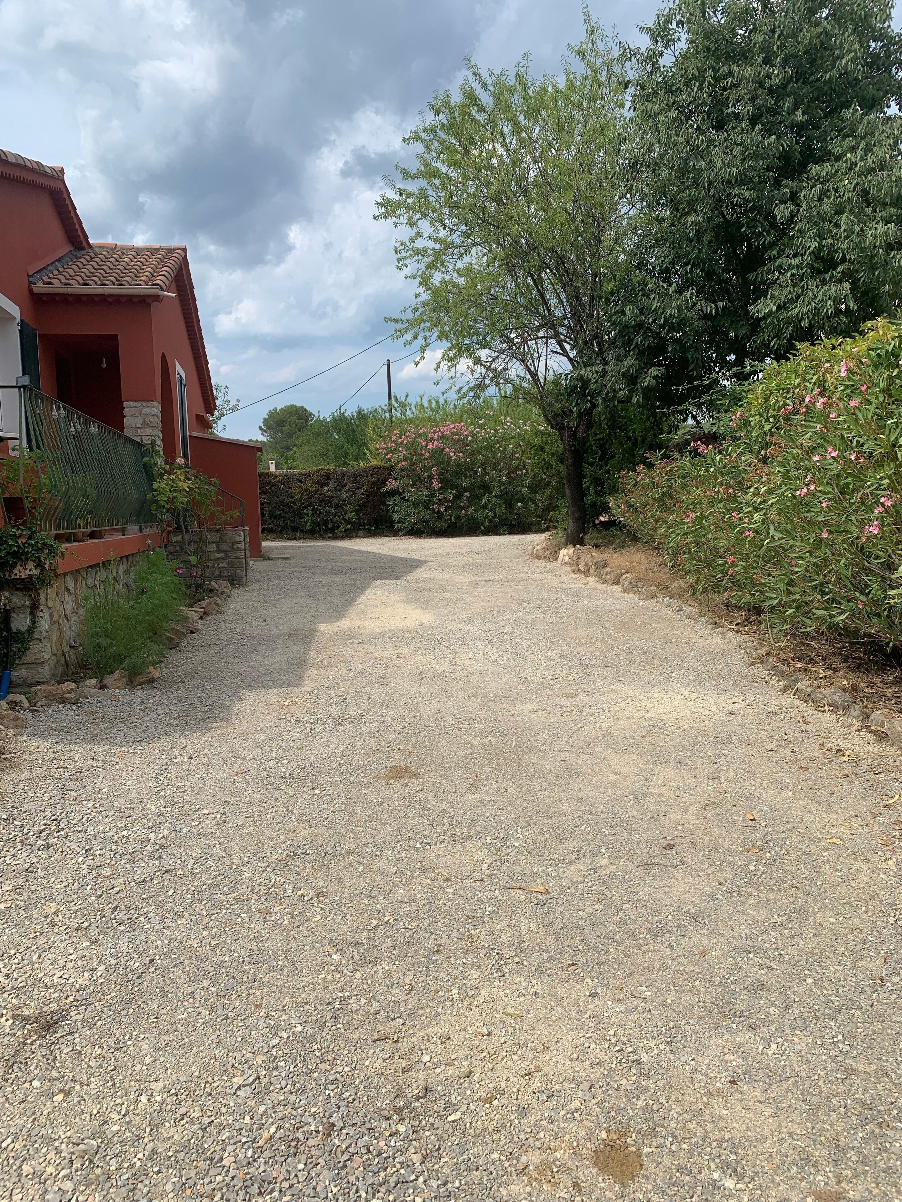 Ein Schotterweg führt zu einem roten Haus mit einer Steinmauer und einem Metallzaun.