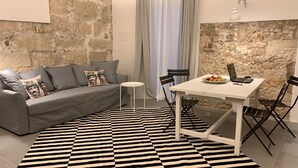 A modern living room with a grey sofa, a small round table, and a white dining table with chairs. A black and white striped rug covers the floor. - Casa Lunya (siracusa)