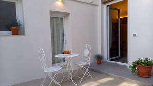 A small patio with a white metal table and chairs, a potted plant, and a sliding glass door leading to an interior space. - Casa Lunya (siracusa)