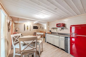 A compact kitchen with a red refrigerator, white cabinets, and a wooden ceiling.