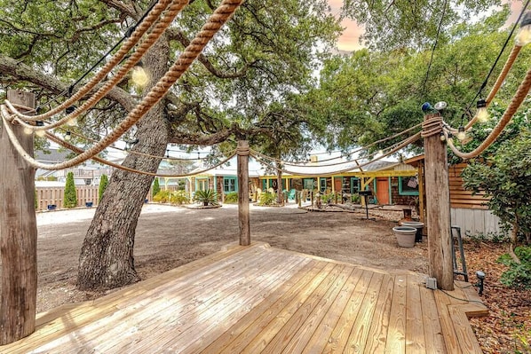 A wooden deck with rope swings and a rustic building with a green door.