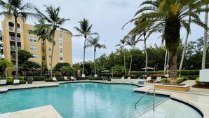 A swimming pool with a curved edge, surrounded by palm trees and a building with balconies. - LUXURY THE YATCH 301- FREE PARKING AND WIFI (Aventura)