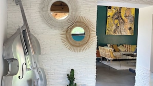 A room with a white brick wall, a large wooden beam ceiling, and a hanging cello. There are two circular mirrors on the wall, a cactus plant, and a sculpture of a giraffe and a rhinoceros. - LE MAS Calisto (TRANS EN PROVENCE)