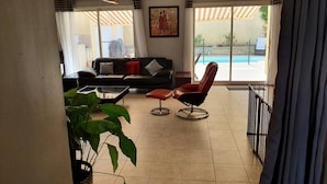 A living room with a black leather sofa, a red armchair, a glass coffee table, and a large potted plant.