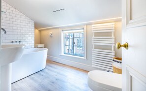 Une salle de bain moderne avec une baignoire sur pieds, une fenêtre avec des stores et un porte-serviettes.