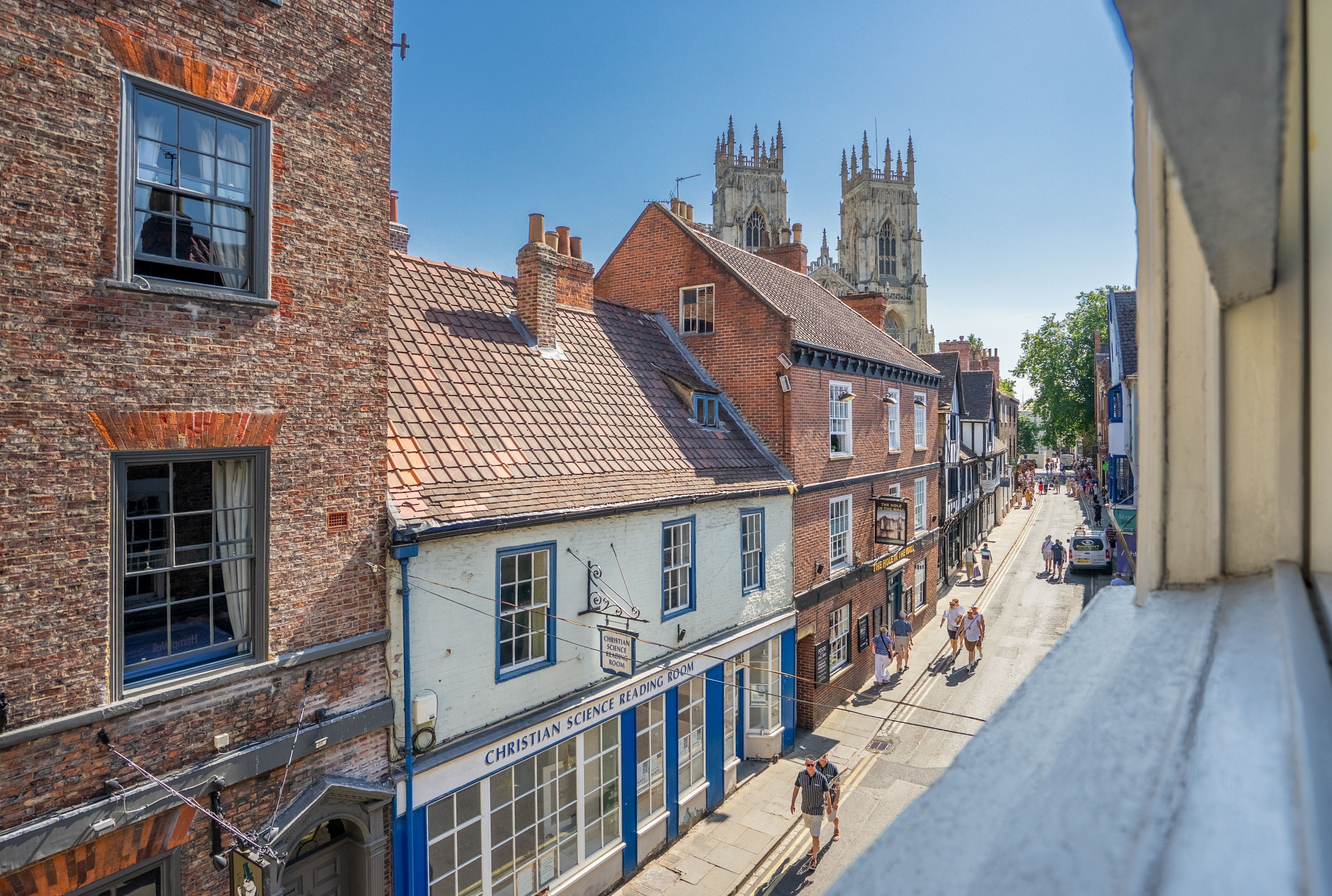 A street view with traditional brick buildings, a church with a tall spire, and a sign for a Christian Science Reading Room.