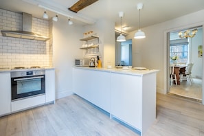 Une cuisine moderne avec des meubles blancs, un four encastré et des luminaires suspendus.