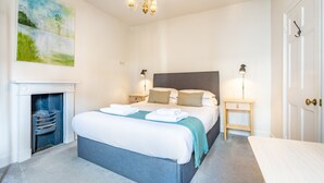 Hotellihuone, jossa on sänky, yöpöydät, takka ja taulu seinällä.