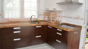 Une cuisine avec des meubles de rangement en bois foncé, un évier en acier inoxydable et une fenêtre ornée de rideaux légers.