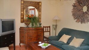 Un salon comprenant une télévision, une commode en bois, un canapé vert et un miroir décoratif.