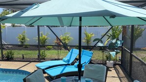Un patio exterior con piscina, sillas de descanso y una mesa lista para comer.