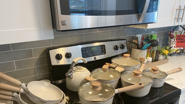 Una cocina con estufa negra, microondas de acero inoxidable y varias ollas y sartenes.