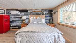 A bedroom with a bed, wooden headboard, a red cabinet, and a window with blinds. - Captain's Quarters at Island Breeze of CB (Carolina Beach)