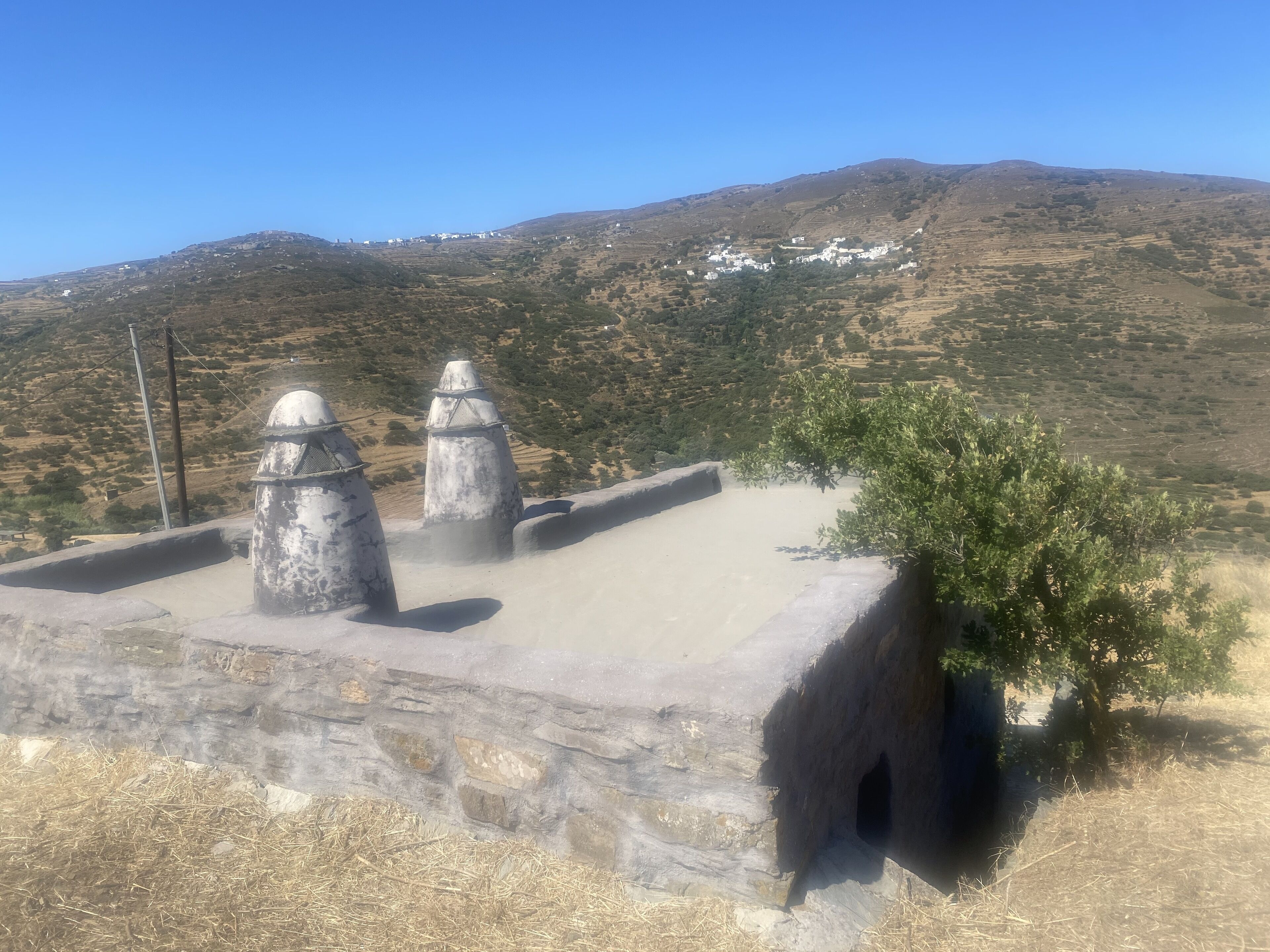 Estructura de piedra con tres techos cónicos, un pequeño árbol y un paisaje montañoso al fondo.