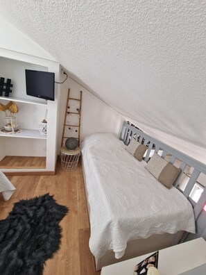 Ein Schlafzimmer mit Schlafbox, einem an der Wand montierten Fernseher, einer Leiter und einem kleinen Regal mit Dekoration.