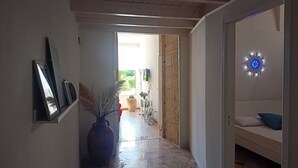 Un pasillo con piso de baldosas, un florero con plantas secas y una cama con almohada azul.