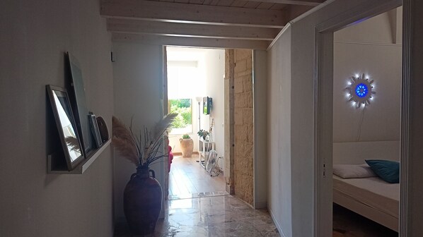 A hallway with a tiled floor, a vase with dried plants, and a bed with a blue pillow.
