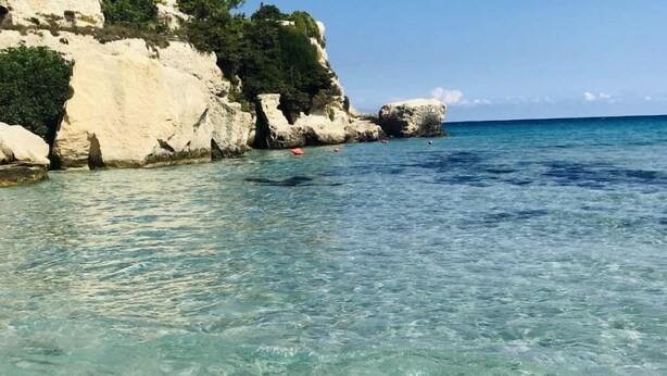 Una playa costera despejada con acantilados rocosos y una pequeña estructura similar a una cueva.