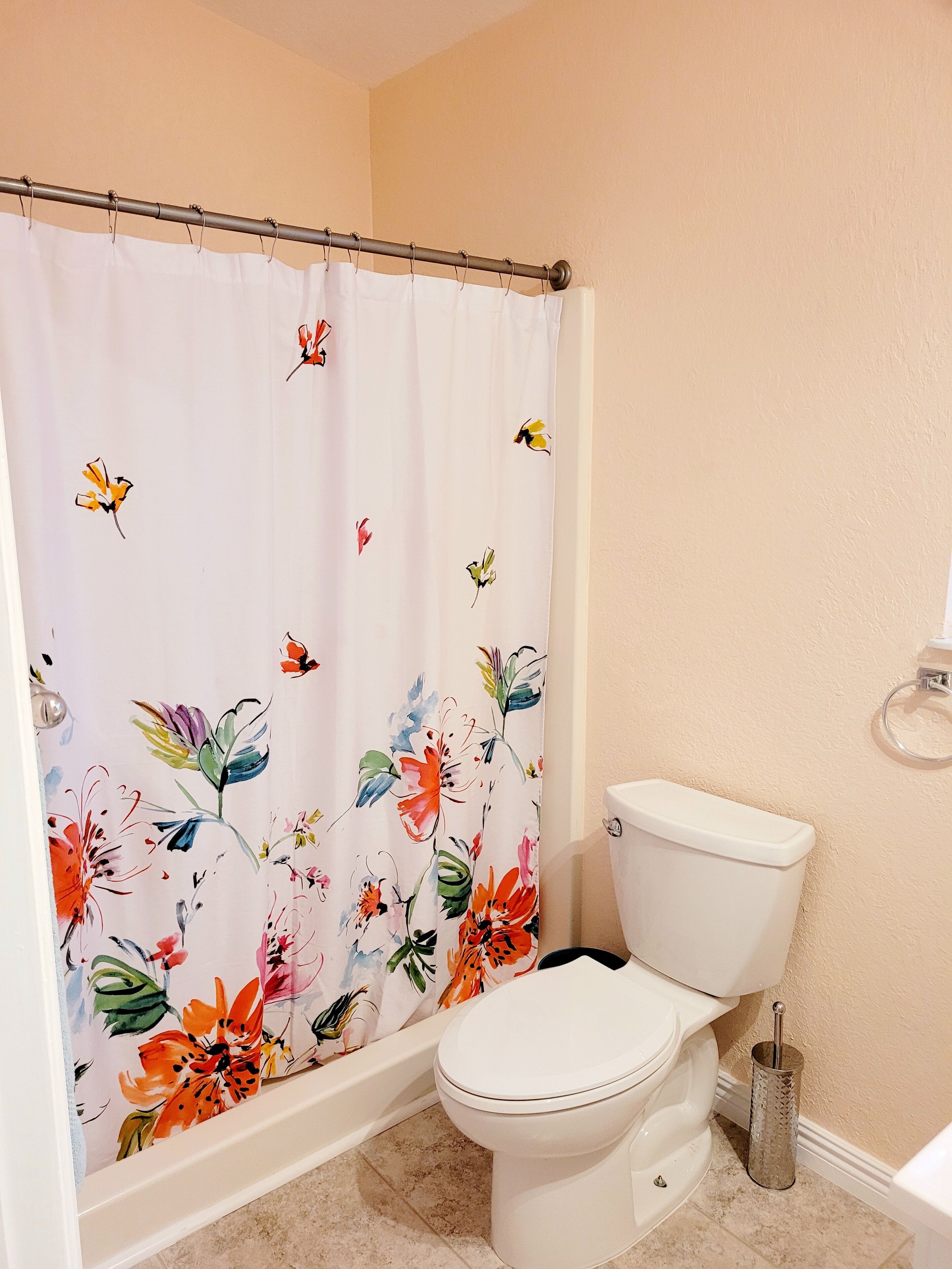 Un baño con inodoro, cortina de ducha con motivos florales y bañera.