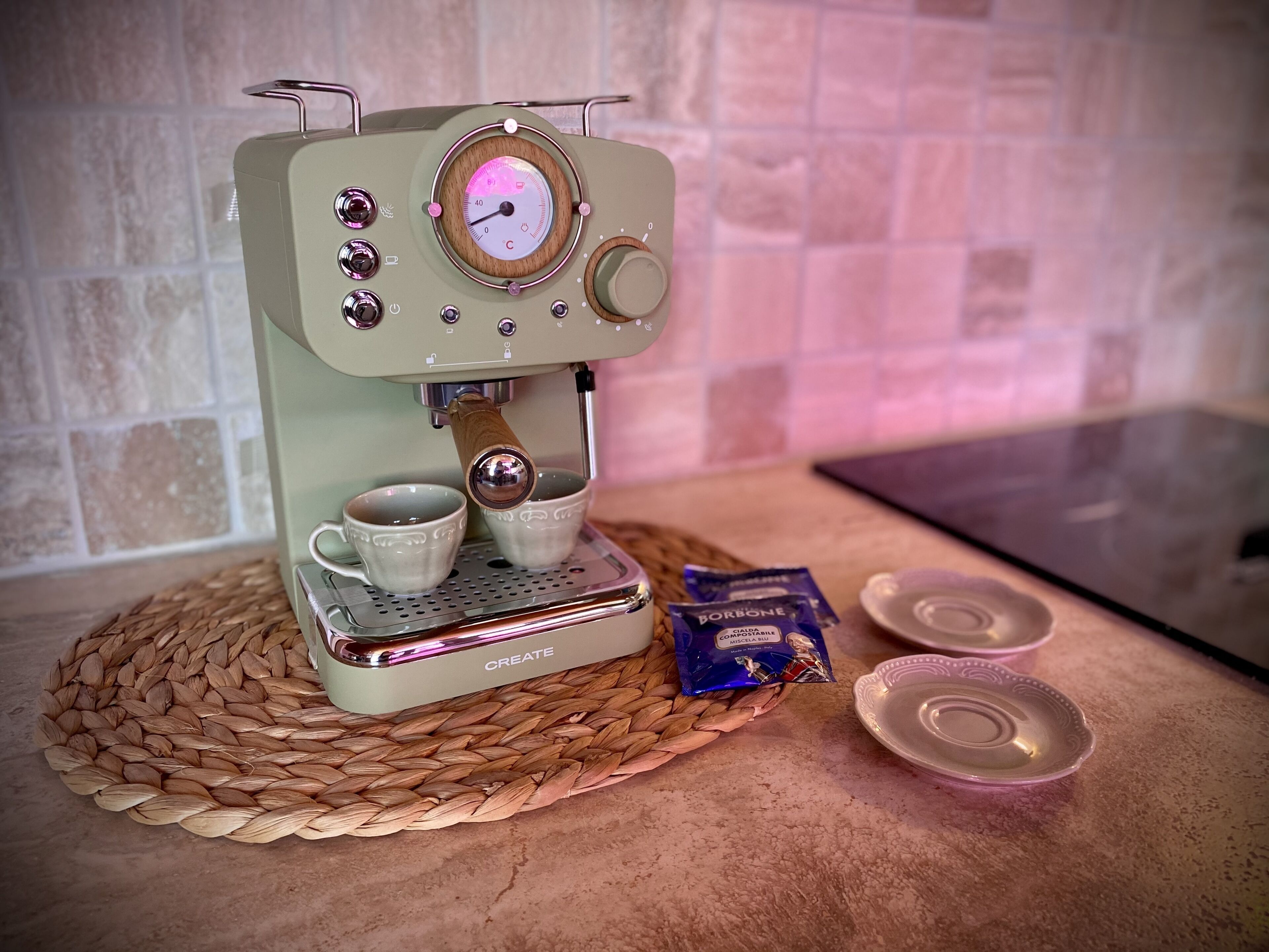 Una macchina da caffè espresso in stile vintage con due tazze sulla sua base, un sottobicchiere intrecciato sotto e due confezioni di capsule di caffè accanto.