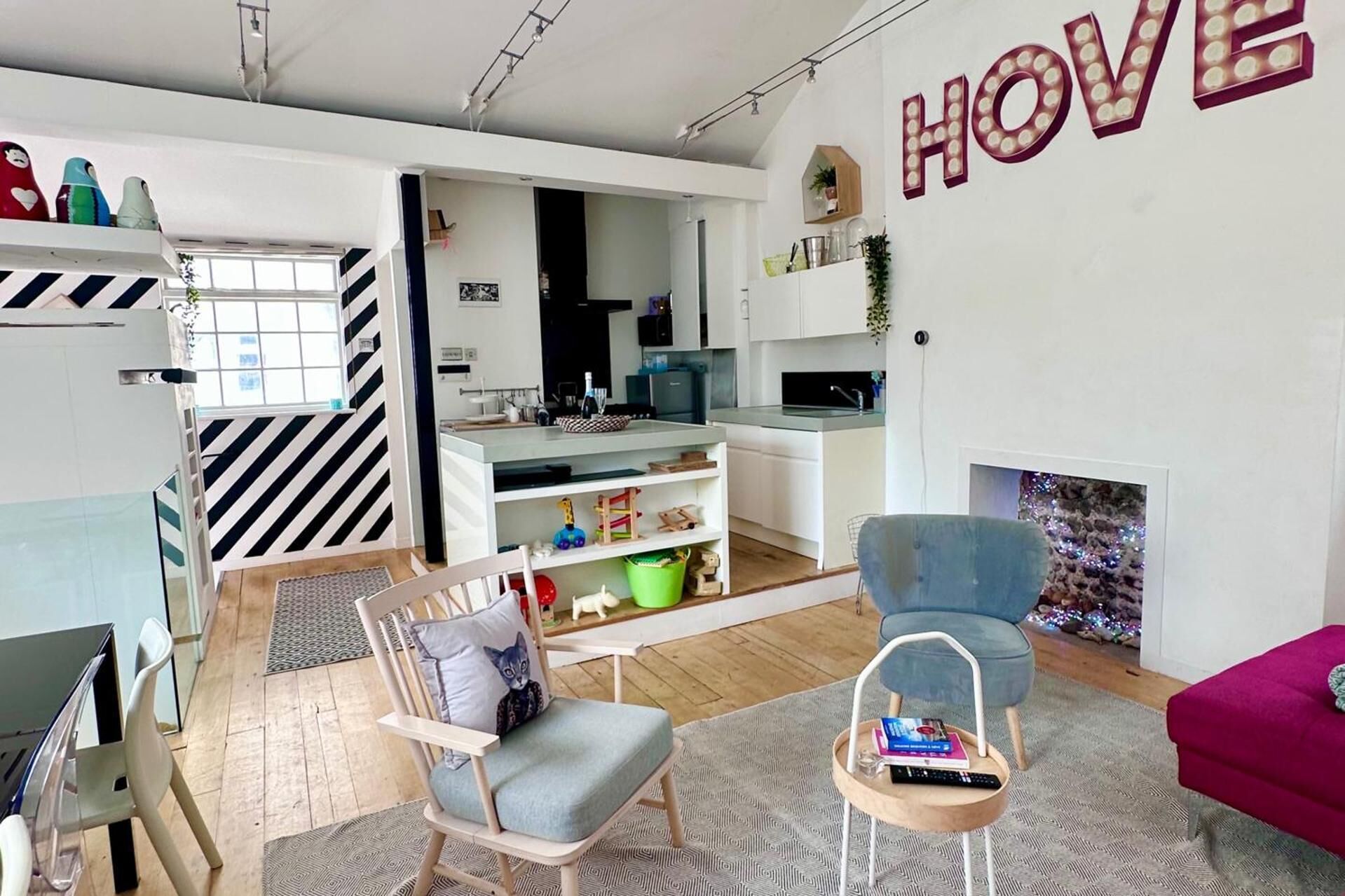 A modern living room with a sofa, a chair, a dining table, and a kitchen area.