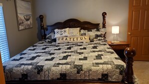 Une chambre à coucher avec une couvre-lit matelassé, une tête de lit en bois, une table de chevet avec une lampe et une porte.
