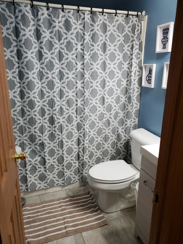 A bathroom with a patterned shower curtain, a toilet, a sink, and a wooden door. - Awesome Waterfront Views, with all the comforts of home. (Oconto)