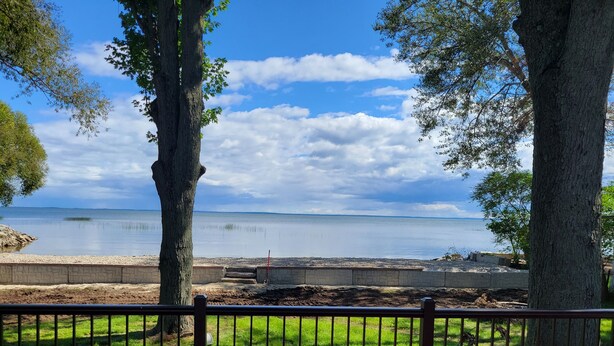 Une vue depuis un balcon donnant sur un lac paisible, avec un mur de pierre et une zone herbeuse au premier plan.