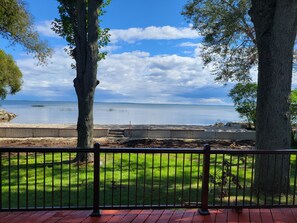 A view from a balcony overlooking a calm lake with a stone wall and grassy area in the foreground. - Awesome Waterfront Views, with all the comforts of home. (Oconto)