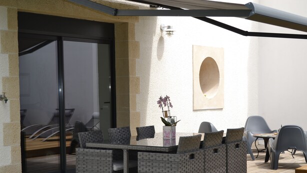 Un patio al aire libre con una mesa de vidrio, sillas de mimbre y una planta en maceta.
