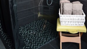 Un espacio de ducha moderno con puerta de cristal, un banco y una cesta de toallas.